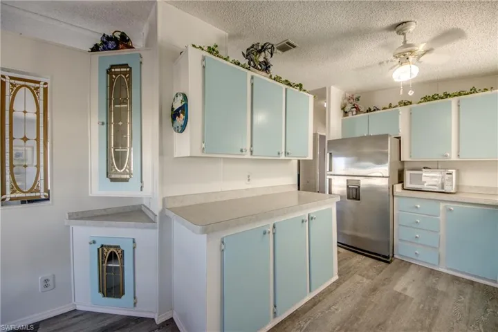 Kitchen with blue cabinets, stainless steel fridge, a textured ceiling, light wood-style flooring, and light countertops