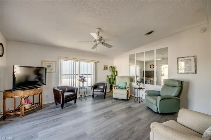 Living area featuring a ceiling fan, a textured ceiling, wood finished floors, and lofted ceiling