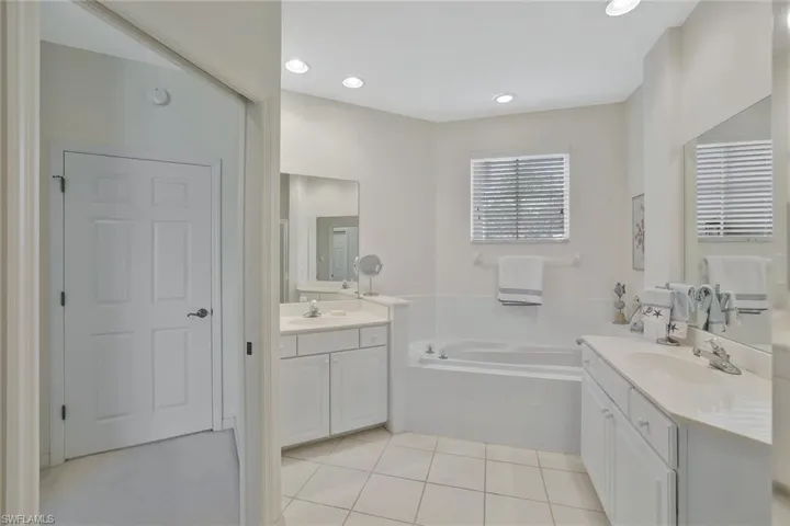 Bathroom featuring two vanities, light tile patterned floors, a garden tub, and recessed lighting