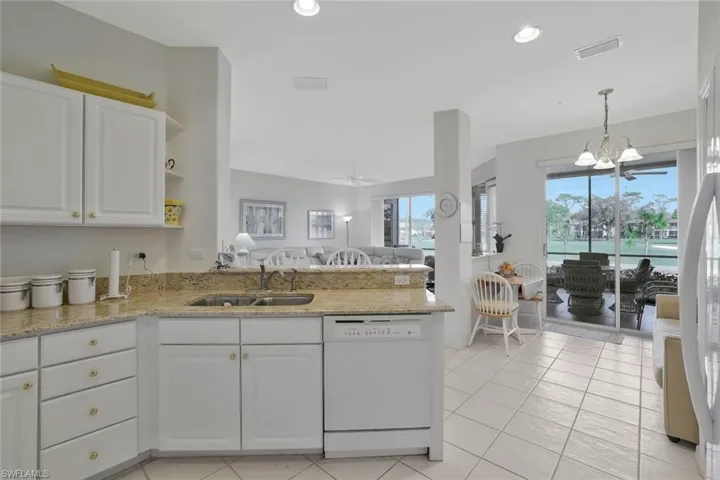 Kitchen featuring light stone counters, open floor plan, white appliances, suspended lighting, and white cabinetry