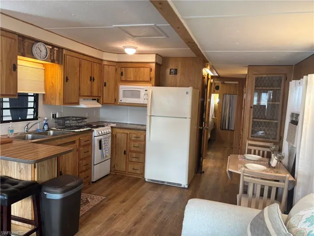 Kitchen featuring brown cabinetry, white appliances, dark wood-style floors, wood walls, and a breakfast bar area