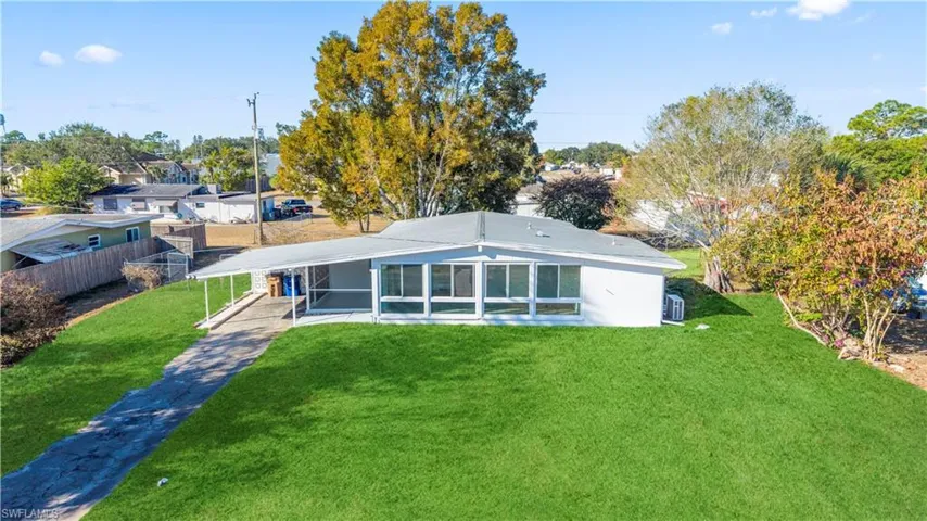 Back of property featuring a sunroom, a carport, a yard, and concrete driveway