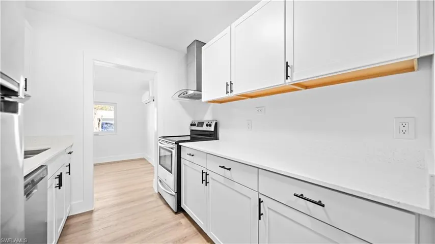 Kitchen featuring stainless steel appliances, white cabinets, light wood-style floors, and light stone counters