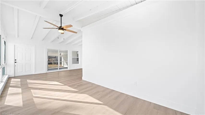 Unfurnished living room featuring ceiling fan, light wood-style flooring, and lofted ceiling with beams