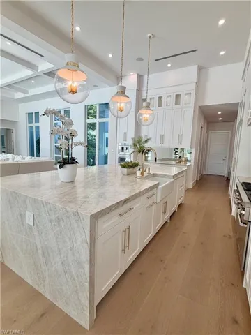 Kitchen with light stone counters, white cabinets, light wood-style flooring, hanging light fixtures, and beamed ceiling