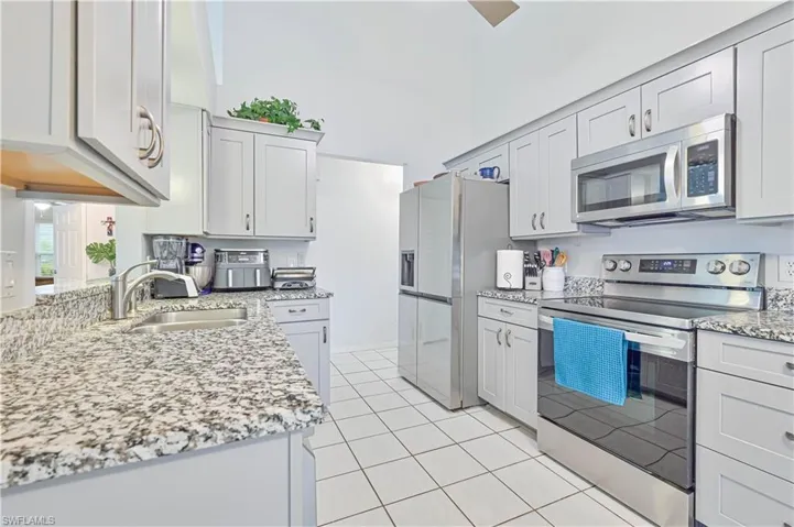 Kitchen with stainless steel appliances, light stone counters, a high ceiling, and light tile patterned flooring