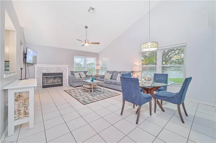 Dining room featuring a ceiling fan, lofted ceiling, a fireplace, and light tile patterned floors