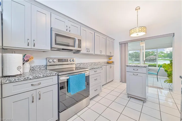 Kitchen with stainless steel appliances, vaulted ceiling, light stone counters, pendant lighting, and light tile patterned floors
