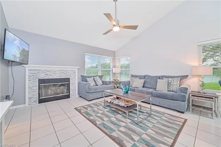 Living area with vaulted ceiling, light tile patterned flooring, a ceiling fan, and a tiled fireplace