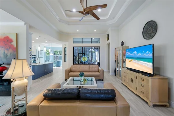 Living room with a high ceiling, ornamental molding, ceiling fan, and light hardwood / wood-style floors