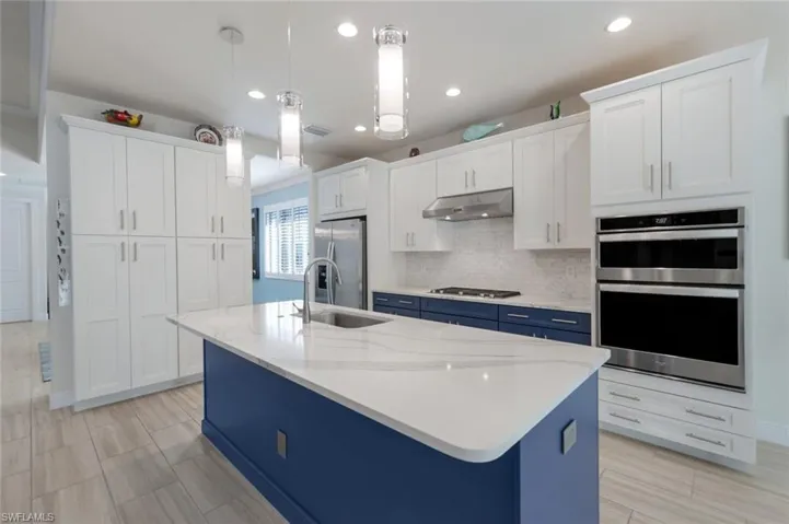 Kitchen featuring decorative light fixtures, sink, white cabinets, stainless steel appliances, and a center island with sink