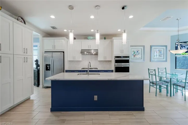 Kitchen featuring appliances with stainless steel finishes, decorative light fixtures, and white cabinets