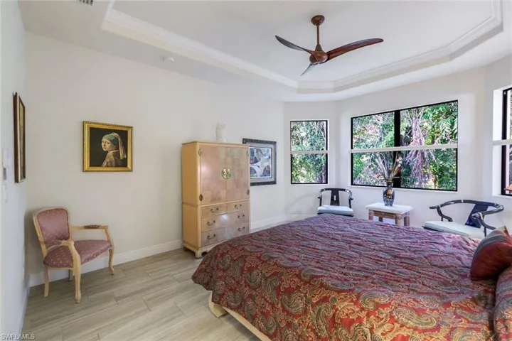 Bedroom with a tray ceiling, ornamental molding, ceiling fan, and light wood-type flooring