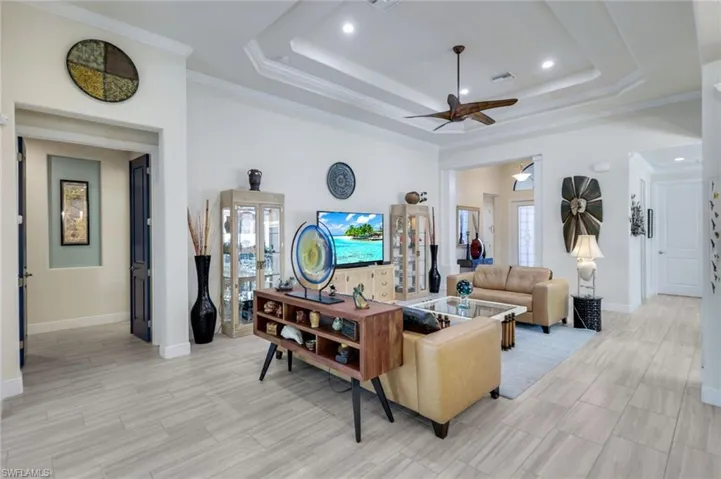 Living room featuring a tray ceiling, ornamental molding, ceiling fan, and light wood-type flooring