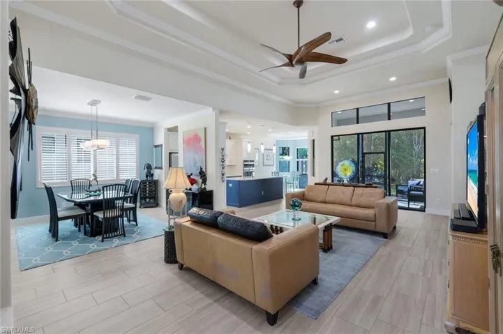 Living room with ceiling fan, ornamental molding, a raised ceiling, and a high ceiling