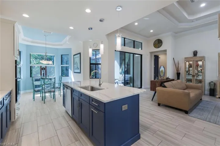 Kitchen with sink, light stone counters, an island with sink, decorative light fixtures, and a raised ceiling