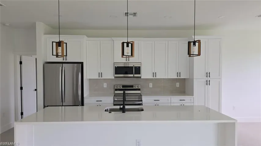 Kitchen featuring stainless steel appliances, hanging light fixtures, light stone countertops, a kitchen island with sink, and white cabinetry
