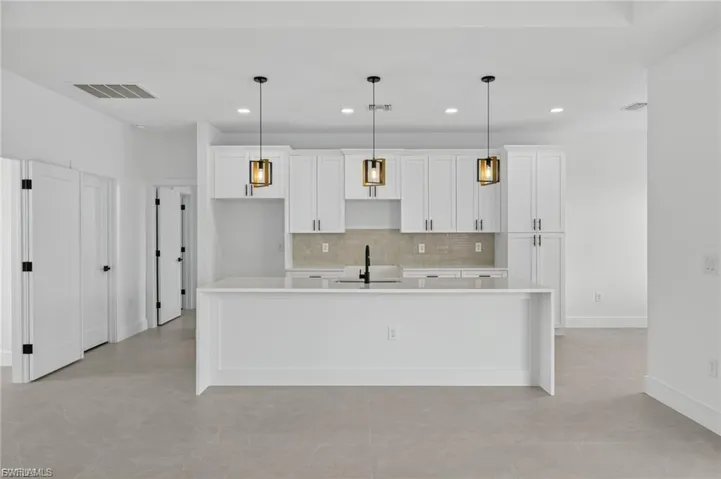Kitchen with white cabinetry, a spacious island, and decorative light fixtures