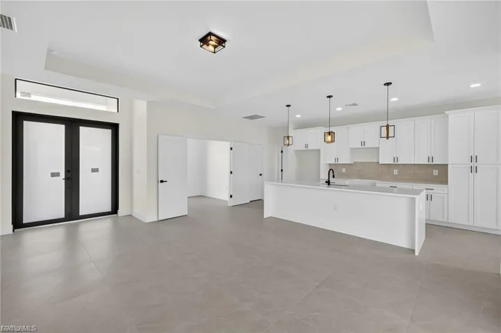 Kitchen with a center island with sink, white cabinets, hanging light fixtures, open floor plan, and tasteful backsplash