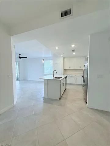Kitchen featuring white cabinetry, ceiling fan, a kitchen island with sink, hanging light fixtures, and open floor plan
