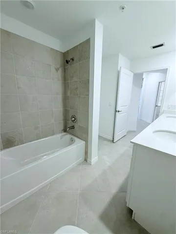 Bathroom with double vanity, shower / washtub combination, and light tile patterned flooring