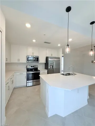 Kitchen featuring stainless steel appliances, pendant lighting, white cabinetry, a center island with sink, and recessed lighting