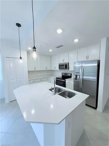 Kitchen featuring stainless steel appliances, white cabinets, a center island with sink, pendant lighting, and light stone countertops