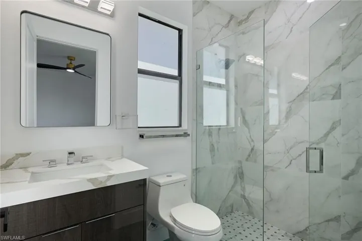 Full bathroom featuring toilet, a marble finish shower, ceiling fan, and vanity