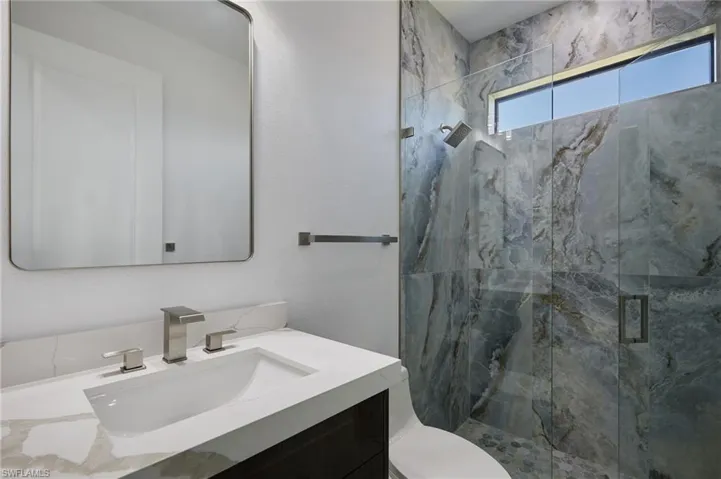 Full bath featuring toilet, vanity, and a marble finish shower