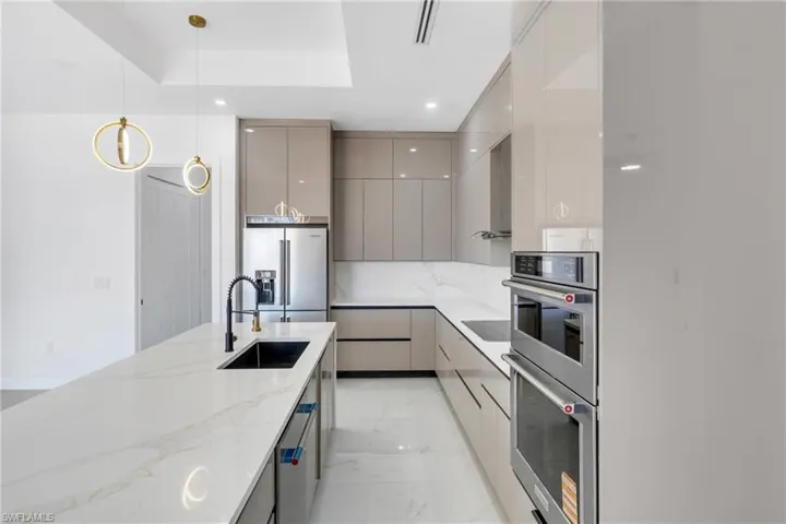 Kitchen with modern cabinets, gray cabinetry, light stone counters, pendant lighting, and stainless steel appliances