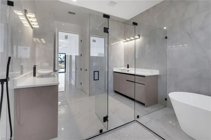 Bathroom featuring light marble finish floors, a freestanding tub, two vanities, a marble finish shower, and tile walls