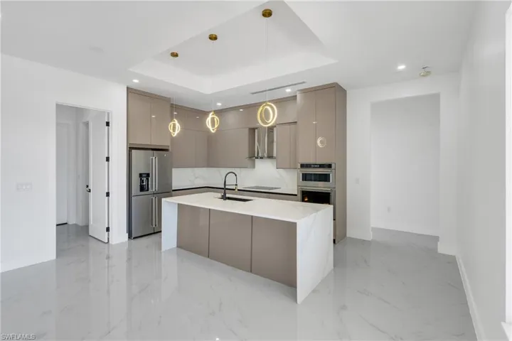 Kitchen featuring modern cabinets, stainless steel appliances, a kitchen island with sink, light stone countertops, and gray cabinetry