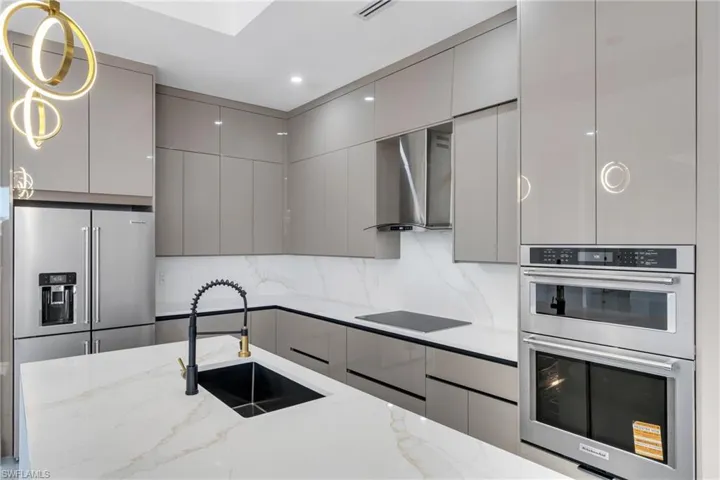 Kitchen featuring modern cabinets, stainless steel appliances, gray cabinets, light stone counters, and recessed lighting