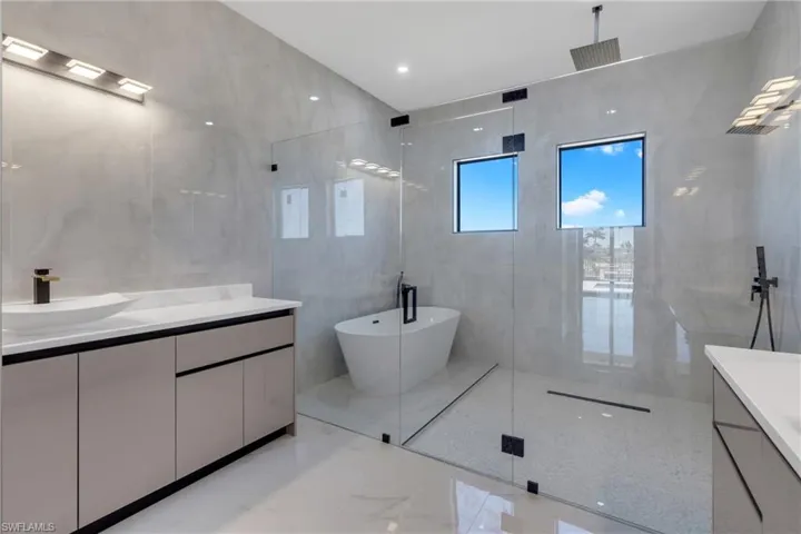 Full bath with vanity, a marble finish shower, a freestanding tub, light marble finish floors, and tile walls