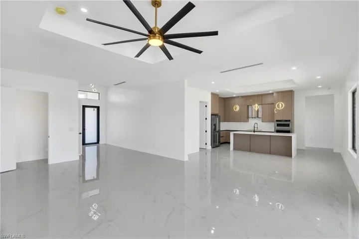 Unfurnished living room with recessed lighting, a tray ceiling, light marble finish floors, and a ceiling fan