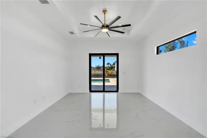Unfurnished room featuring light marble finish floors, a ceiling fan, and a tray ceiling