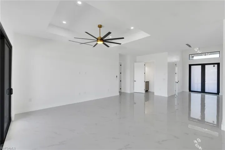 Unfurnished living room with light marble finish flooring, ceiling fan, a raised ceiling, french doors, and recessed lighting