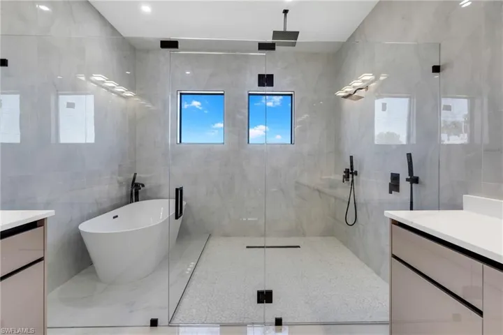 Bathroom featuring vanity, a marble finish shower, tile walls, and a freestanding bath