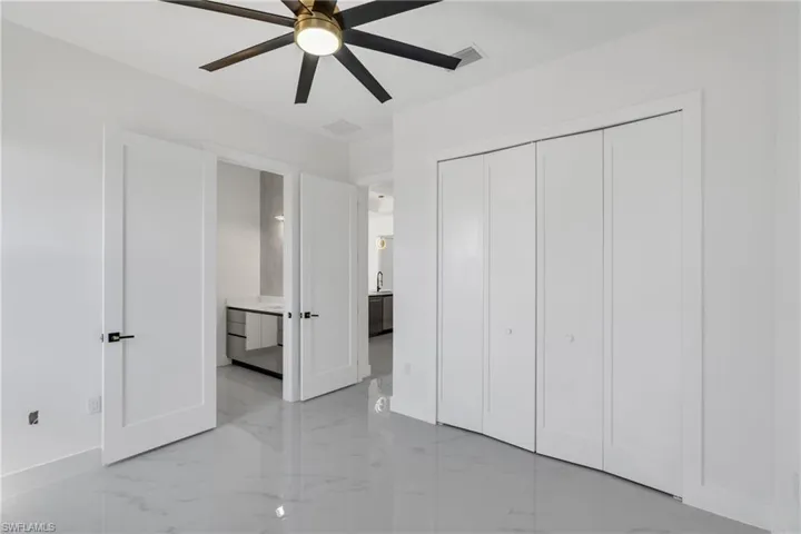 Unfurnished bedroom with light marble finish flooring, ensuite bathroom, a ceiling fan, and a closet