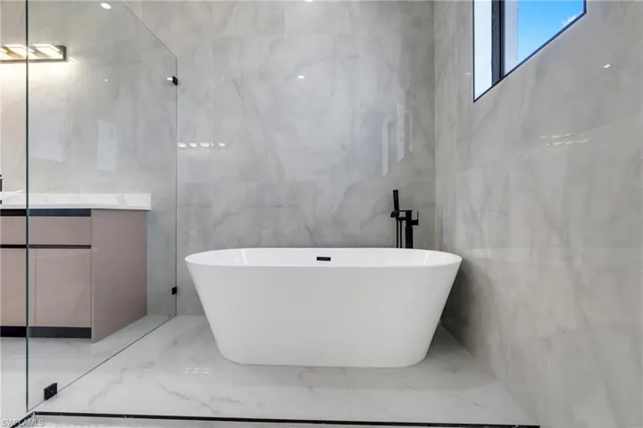 Bathroom with vanity, tile walls, a soaking tub, and light marble finish floors