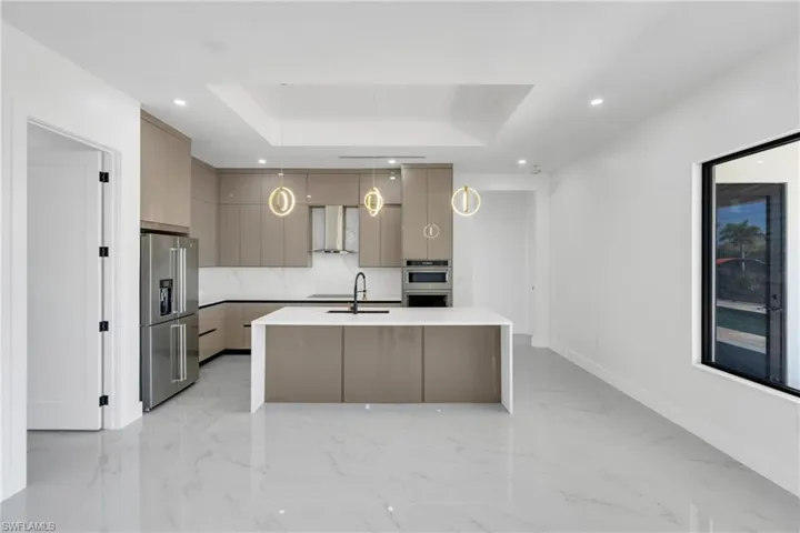 Kitchen with modern cabinets, a raised ceiling, gray cabinets, decorative light fixtures, and stainless steel appliances