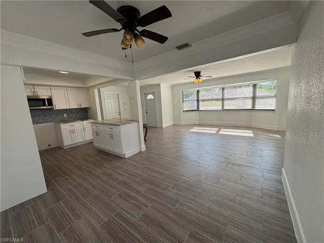 Kitchen featuring white cabinetry, crown molding, ceiling fan, light stone countertops, and open floor plan