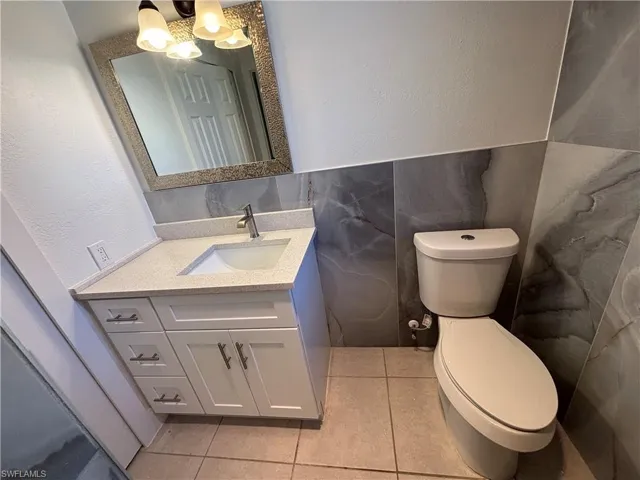 Half bathroom with vanity, a textured wall, light tile patterned floors, and tile walls