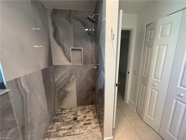 Full bathroom with a marble finish shower and light tile patterned floors