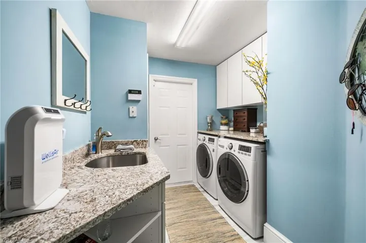 Clothes washing area featuring sink, cabinets, washer and dryer, and light wood-type flooring