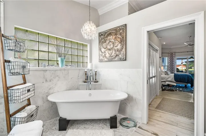 Bathroom with tile walls, hardwood / wood-style floors, a chandelier, and ornamental molding