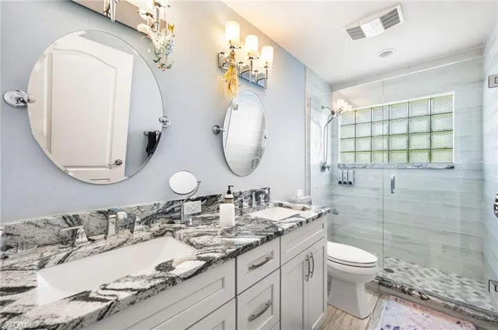 Bathroom with dual vanity, toilet, and an enclosed shower