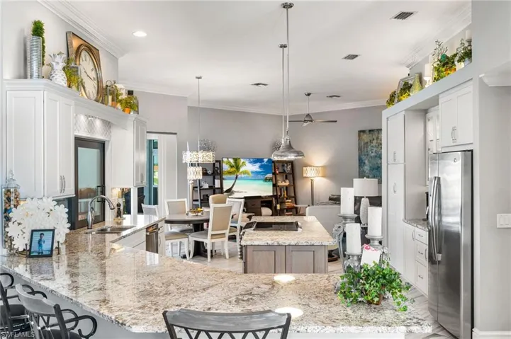 Kitchen featuring hanging light fixtures, appliances with stainless steel finishes, white cabinets, and light stone countertops