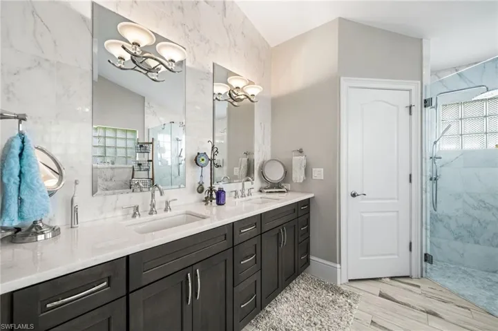 Bathroom with a notable chandelier, a wealth of natural light, double sink vanity, and walk in shower