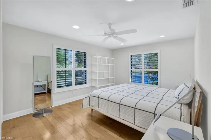 The furnished main en suite bedroom features that gorgeous maple flooring, multiple windows for light, a ceiling fan, plus custom built in closet details.